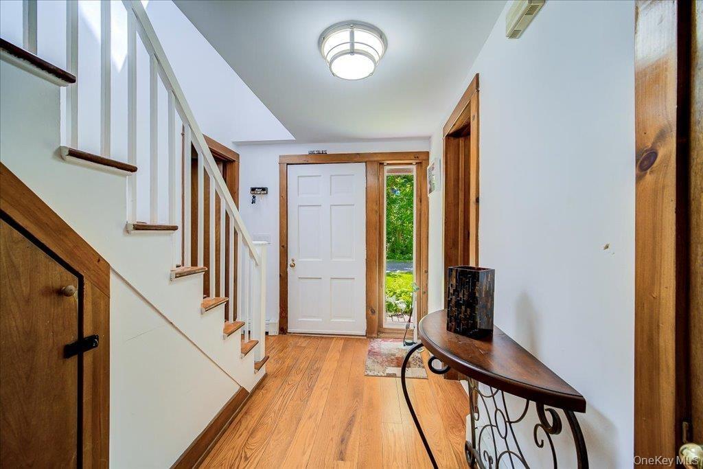 Foyer featuring wood-finish flooring, a white paneled entry door with sidelight, natural wood trim, and a staircase with white risers and wood treads