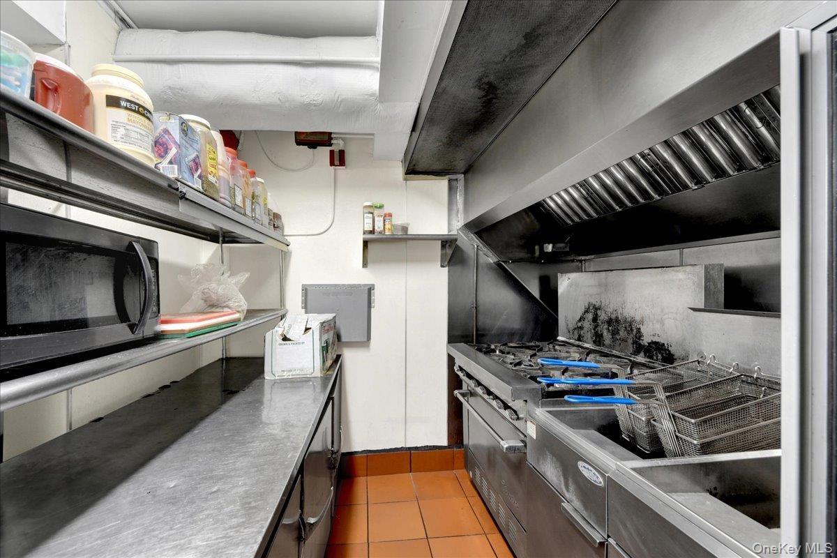 Commercial-grade stainless steel range with integrated fryer station, stainless steel exhaust hood, and industrial shelving