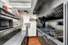 Commercial-grade stainless steel range with integrated fryer station, stainless steel exhaust hood, and industrial shelving