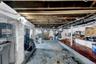 Storage space with exposed ceiling joists and support beams, featuring a painted brick wall, concrete flooring, and visible utility lines