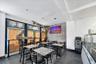 Commercial dining area featuring multiple tables and chairs, white subway tile wall, large display screen, and a service counter with glass enclosure