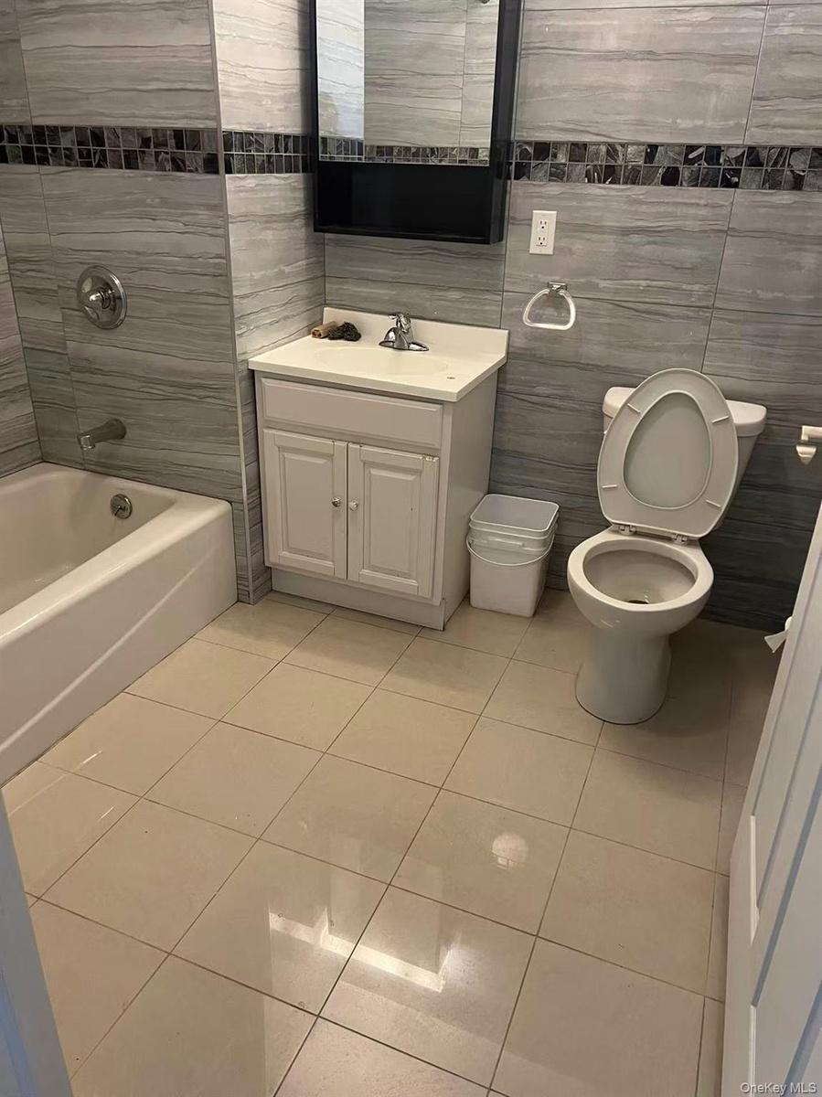 Bathroom featuring tile patterned flooring, toilet, vanity, tile walls, and washtub / shower combination