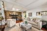Spacious living area featuring a stone fireplace, wood-finish flooring, exposed ceiling beams, and a pass-through window