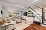 Living area featuring wood-finish flooring, exposed ceiling beams, and a modern staircase with dark treads and a black handrail