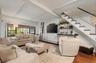 Open-concept living area featuring exposed ceiling beams, wood-finish flooring, and a staircase with painted risers