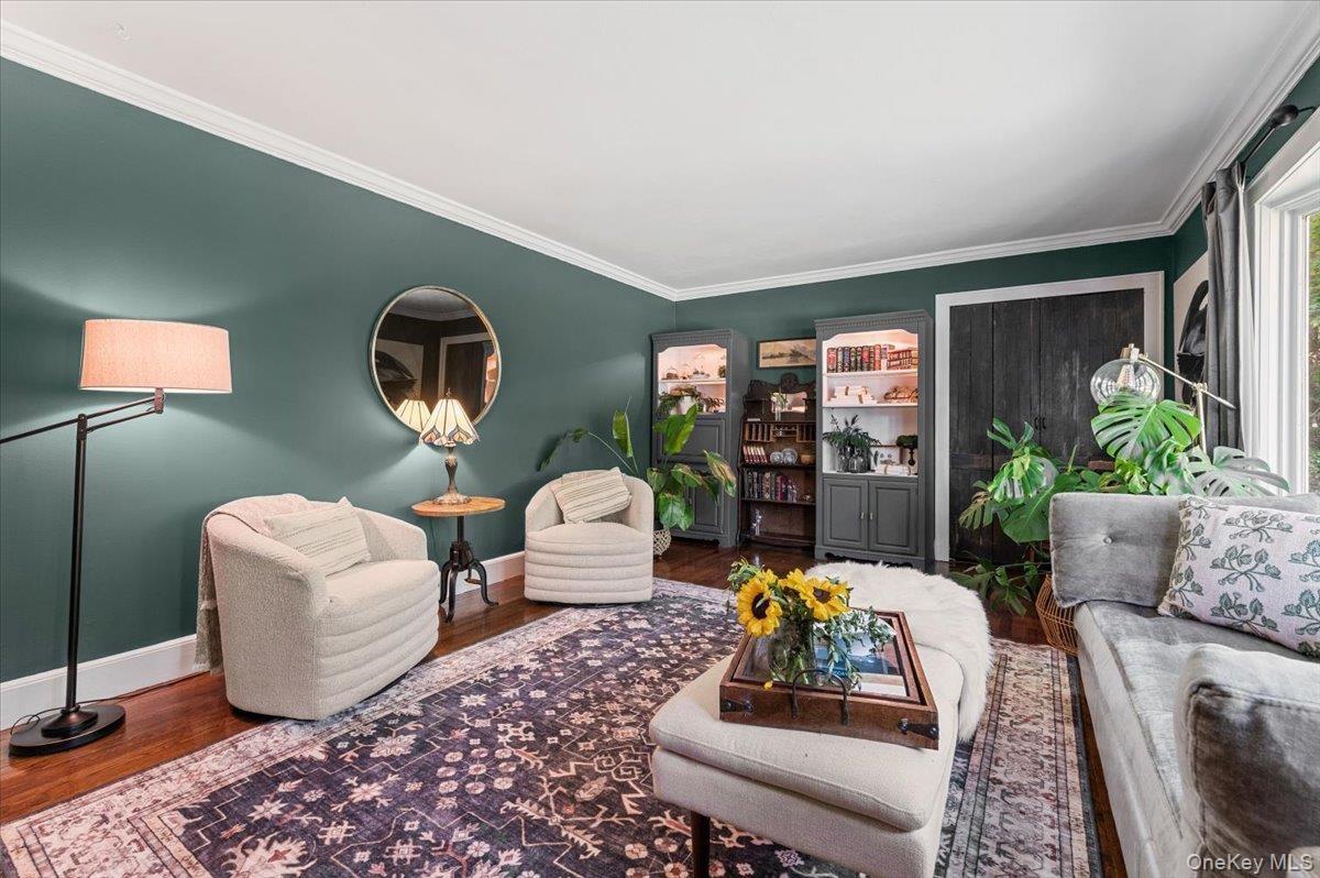 Spacious room featuring wood-finish flooring, deep green painted walls, white crown molding, and built-in shelving units with glass doors