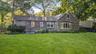 Expansive green lawn, wood shake siding, multiple windows, and a prominent bay window
