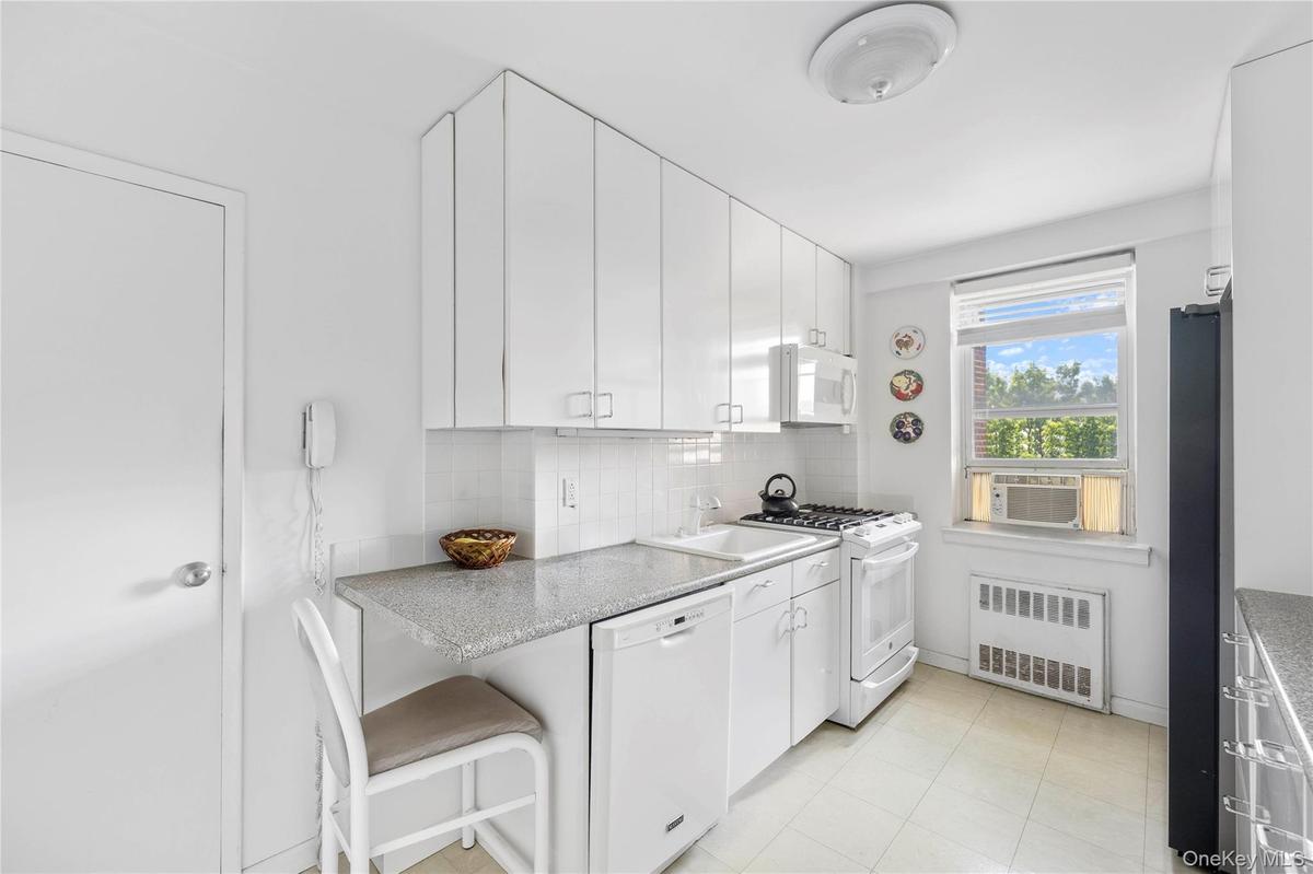 Kitchen featuring white cabinetry with silver hardware, speckled countertops, a white tile backsplash, and linoleum flooring