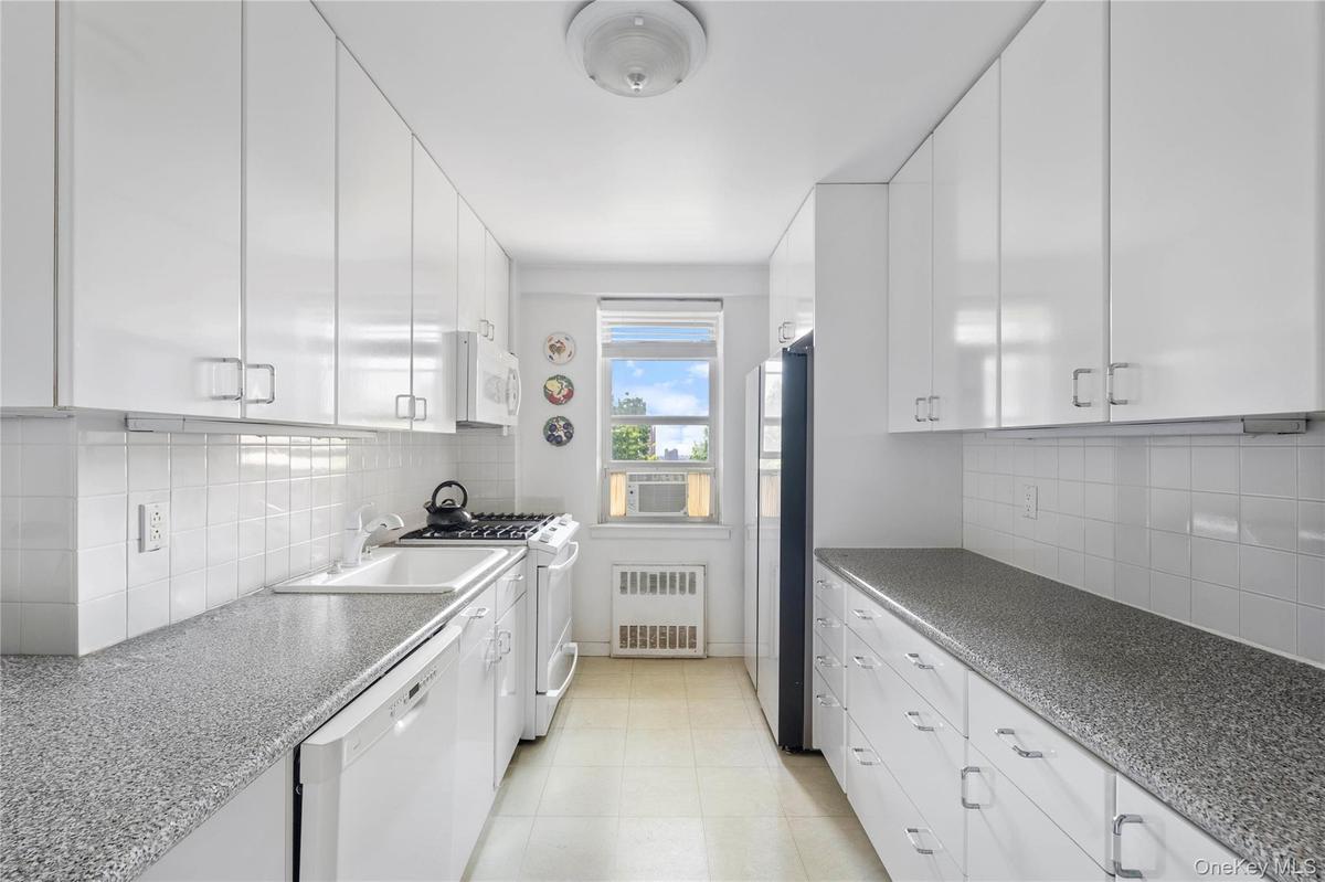 Galley kitchen featuring abundant white cabinetry, a white tile backsplash, and speckled countertops