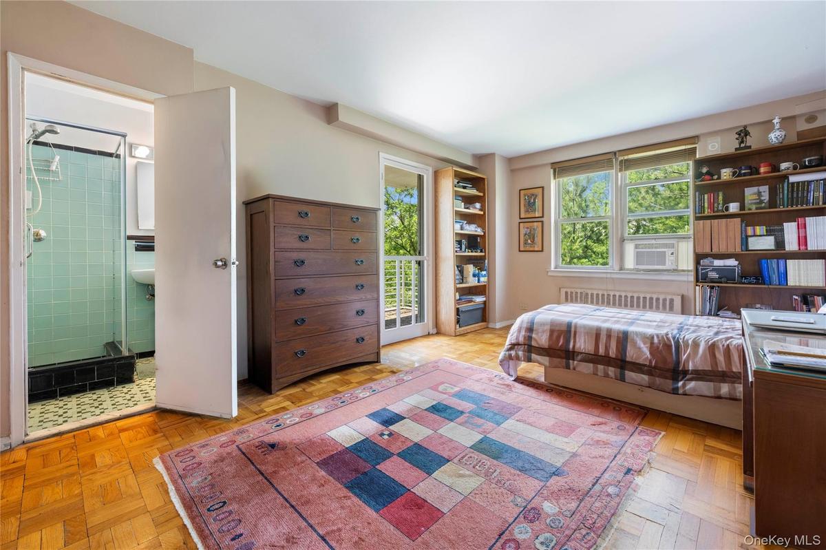 Hardwood parquet flooring throughout the room, featuring a built-in shelving unit, a window with exterior views, and a glass-paneled door leading to a