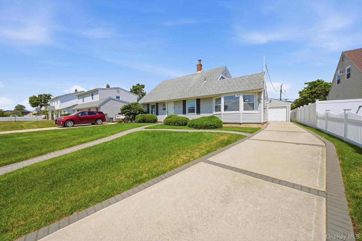 Light-colored siding exterior with a pitched roof, featuring a multi-segment concrete driveway with paver accents leading to a detached garage