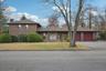 View of front of property with brick siding, asphalt driveway, a chimney, a front lawn, and an attached garage
