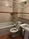 Bathroom featuring tiled shower / bath combo, toilet, and tile walls