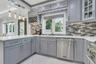 Contemporary kitchen featuring light gray cabinetry, white quartz countertops, undermount lighting, coutner seating