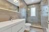 Modern bathroom featuring a white vanity with an integrated sink, a frameless lighted, anti fog mirror, and a glass-enclosed shower with porcelain til