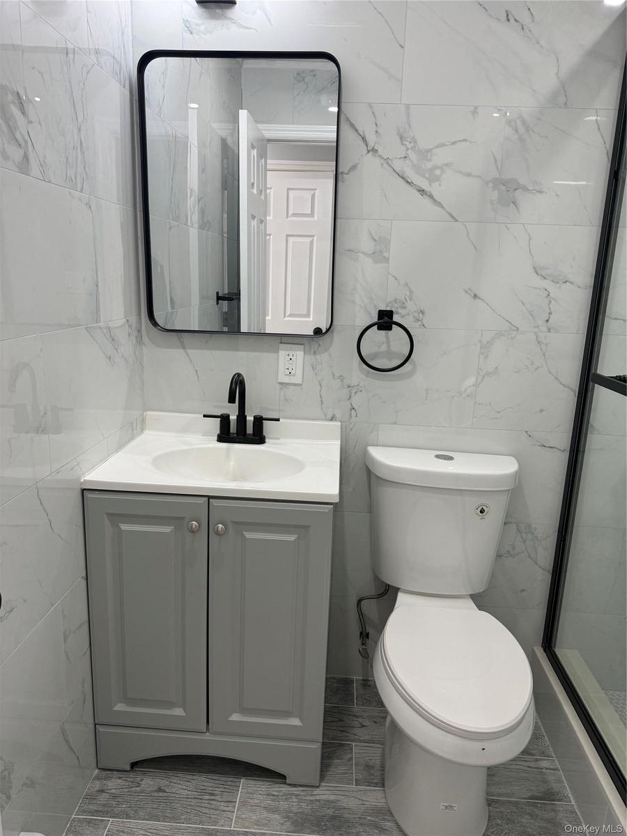 Full bath with tile walls, vanity, and a marble finish shower