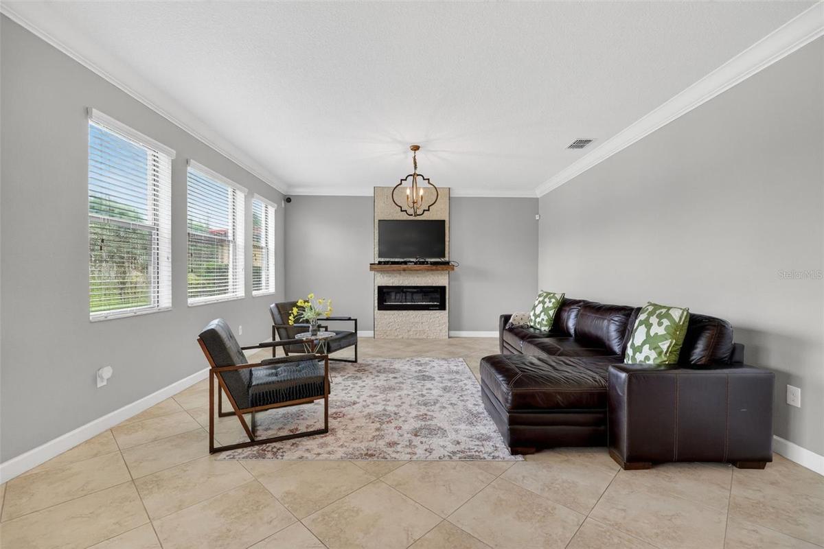 Living Room with Crown Molding, 3 Stunning Windows, Accent Wall with Stone Accent and Chandelier.
