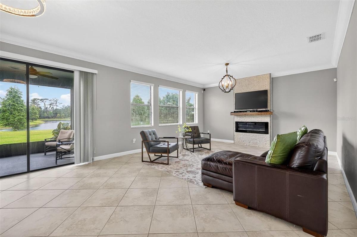 View of Double Sliding Glass Doors and Living Room with Crown Molding, 3 Stunning Windows, Accent Wall with Stone Accent and Chandelier.