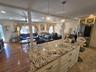 Spacious open-concept interior featuring a large kitchen island with a speckled countertop and cream-colored cabinetry, two crystal pendant lights, re