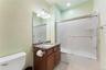 Full bathroom featuring a dark wood-finish vanity with a granite countertop and integrated sink, a large mirror, and a full-size bathtub with a slidin