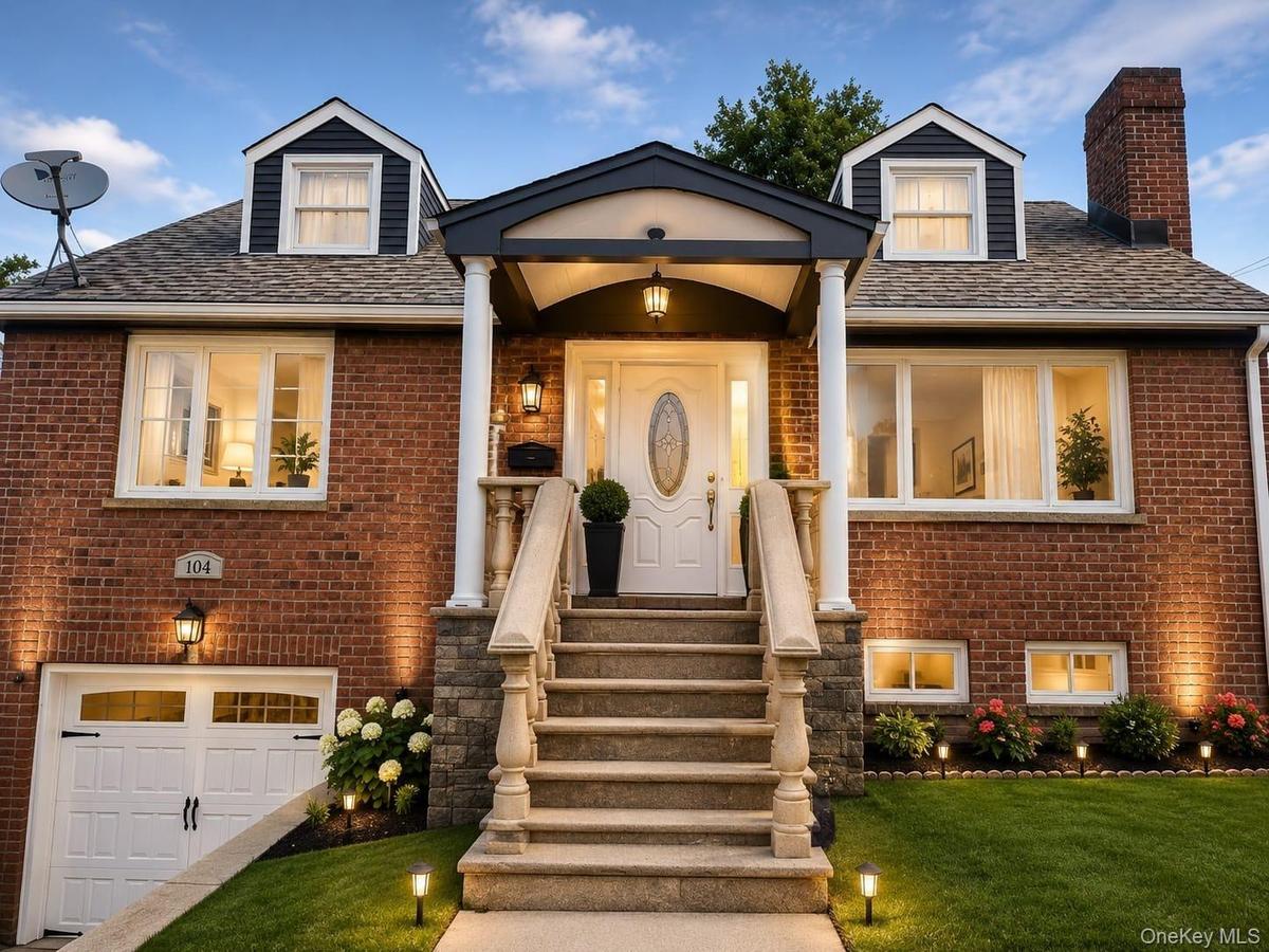 Brick exterior with dormer windows and a covered entry, featuring a stone staircase with balusters