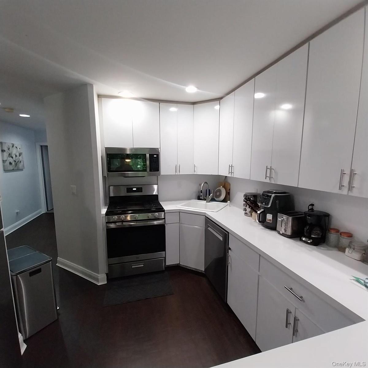 Modern kitchen featuring bright white cabinetry, stainless steel appliances, white countertops, and dark wood-finish flooring
