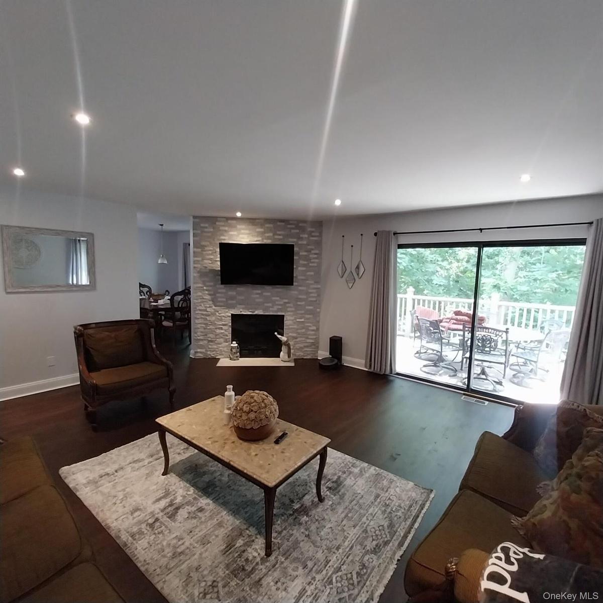 Spacious living area featuring wood-finish flooring, a stone-accented fireplace, and recessed lighting