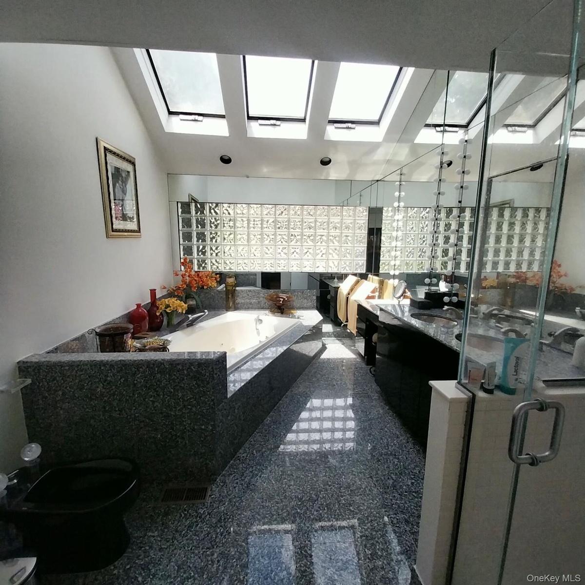 Bathroom featuring multiple skylights, a built-in tub with a stone surround, a glass block wall, and reflective flooring