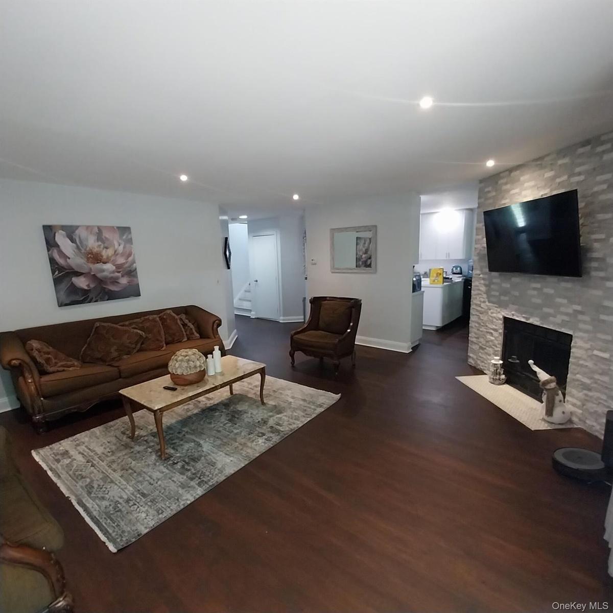Spacious living area featuring rich wood-finish flooring, recessed lighting, and a stone-clad fireplace with a hearth