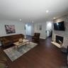 Spacious living area featuring rich wood-finish flooring, recessed lighting, and a stone-clad fireplace with a hearth