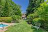 Expansive backyard featuring a manicured lawn, established shrubbery, and mature trees