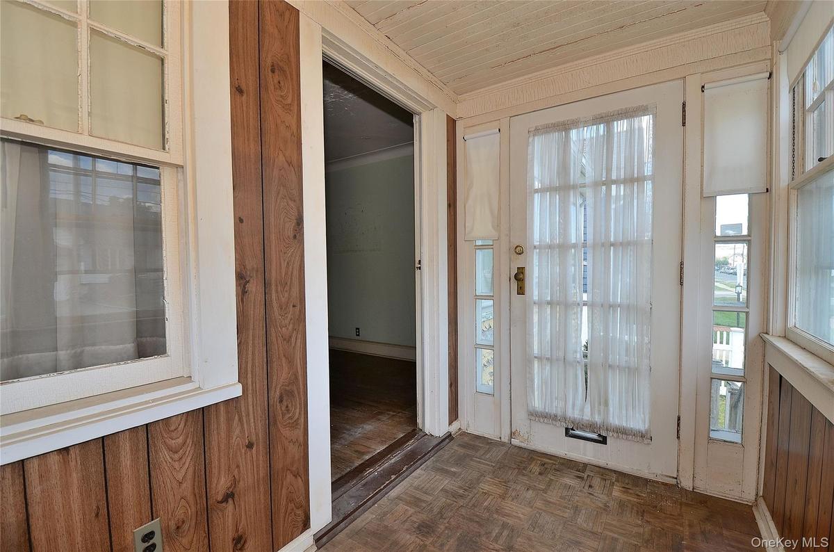Entry featuring multiple windows with roller shades, wood-finish flooring, and horizontal wood paneling