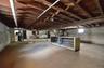 Spacious basement featuring exposed wood ceiling joists and support beams, concrete flooring, concrete block walls, and a visible utility area