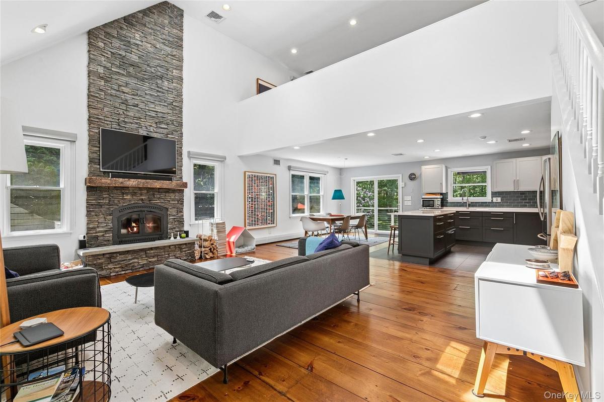 Vaulted ceiling great room featuring a floor-to-ceiling stone fireplace, wood-finish flooring, and a mezzanine overlook