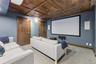 Media room featuring a large projection screen, two in-wall speakers, wood-paneled ceiling, and a patterned carpet