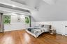 Spacious room featuring exposed ceiling beams, two windows, and wide plank wood flooring