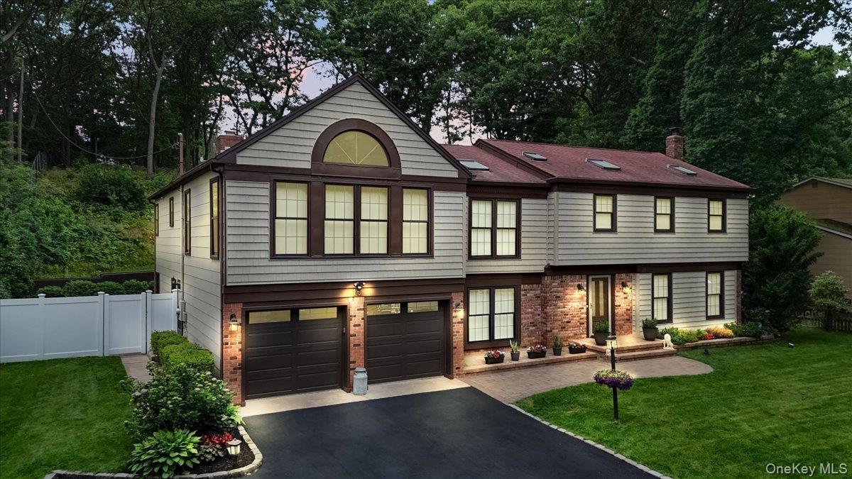 Two-story residence featuring light-toned siding with dark trim, a red-toned roofline with skylights, and a brick facade accent