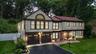 Two-story residence featuring light-toned siding with dark trim, a red-toned roofline with skylights, and a brick facade accent