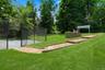 Spacious green lawn featuring a tennis court/ with black chain-link fencing, a multi-tiered paver pathway, a stone retaining wall, and a white pergola