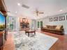 Spacious living area featuring a brick-surround fireplace with a stone hearth, wood-finish flooring, recessed lighting, and a ceiling fan