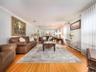 Spacious living area featuring polished wood-finish flooring, a decorative area rug, mirrored wall paneling, and crown molding