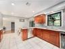 Kitchen featuring tiled flooring, wood cabinetry, stone countertops, a stainless steel dishwasher, and recessed lighting