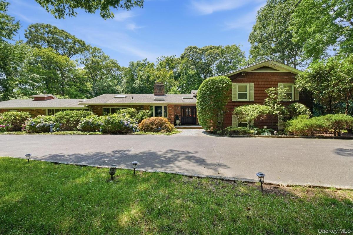 Ranch-style residence featuring a brick facade with cedar shake siding, a multi-car driveway, and integrated outdoor lighting