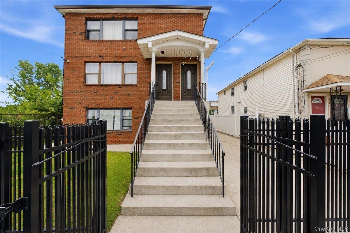 Brick multi-story building featuring multiple entry doors, a covered porch with recessed lighting, and a concrete staircase with black metal railings