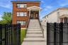 Brick multi-story building featuring multiple entry doors, a covered porch with recessed lighting, and a concrete staircase with black metal railings