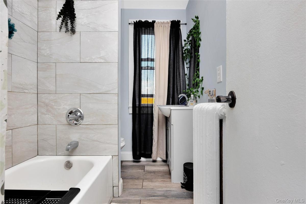 Bathroom with wood finished floors, shower / tub combination, radiator heating unit, and vanity
