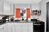 Kitchen with range with gas stovetop, stainless steel microwave, tasteful backsplash, dark stone counters, and white cabinetry