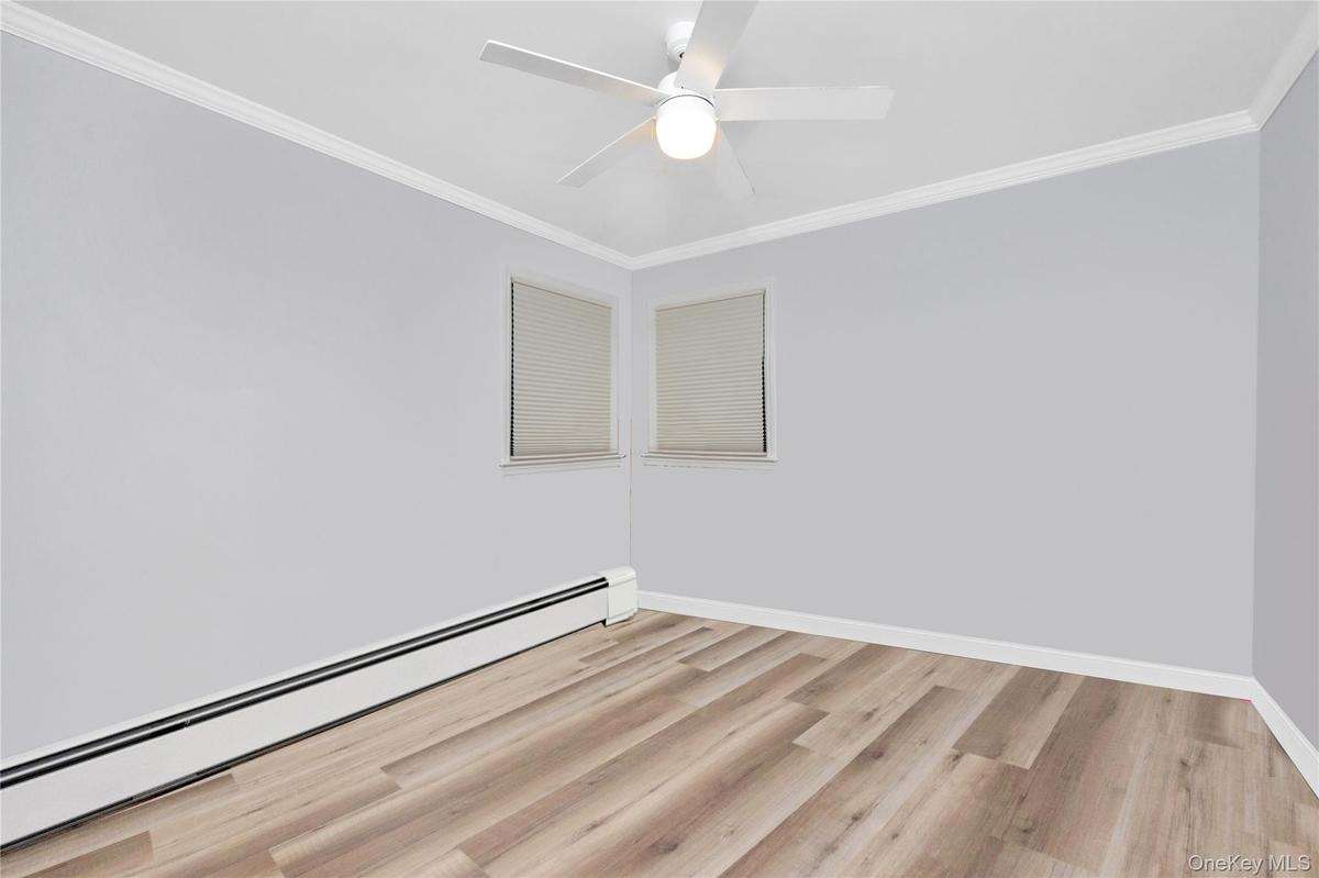Empty room featuring a baseboard radiator, light wood-style floors, crown molding, and ceiling fan
