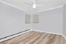 Empty room featuring a baseboard radiator, light wood-style floors, crown molding, and ceiling fan