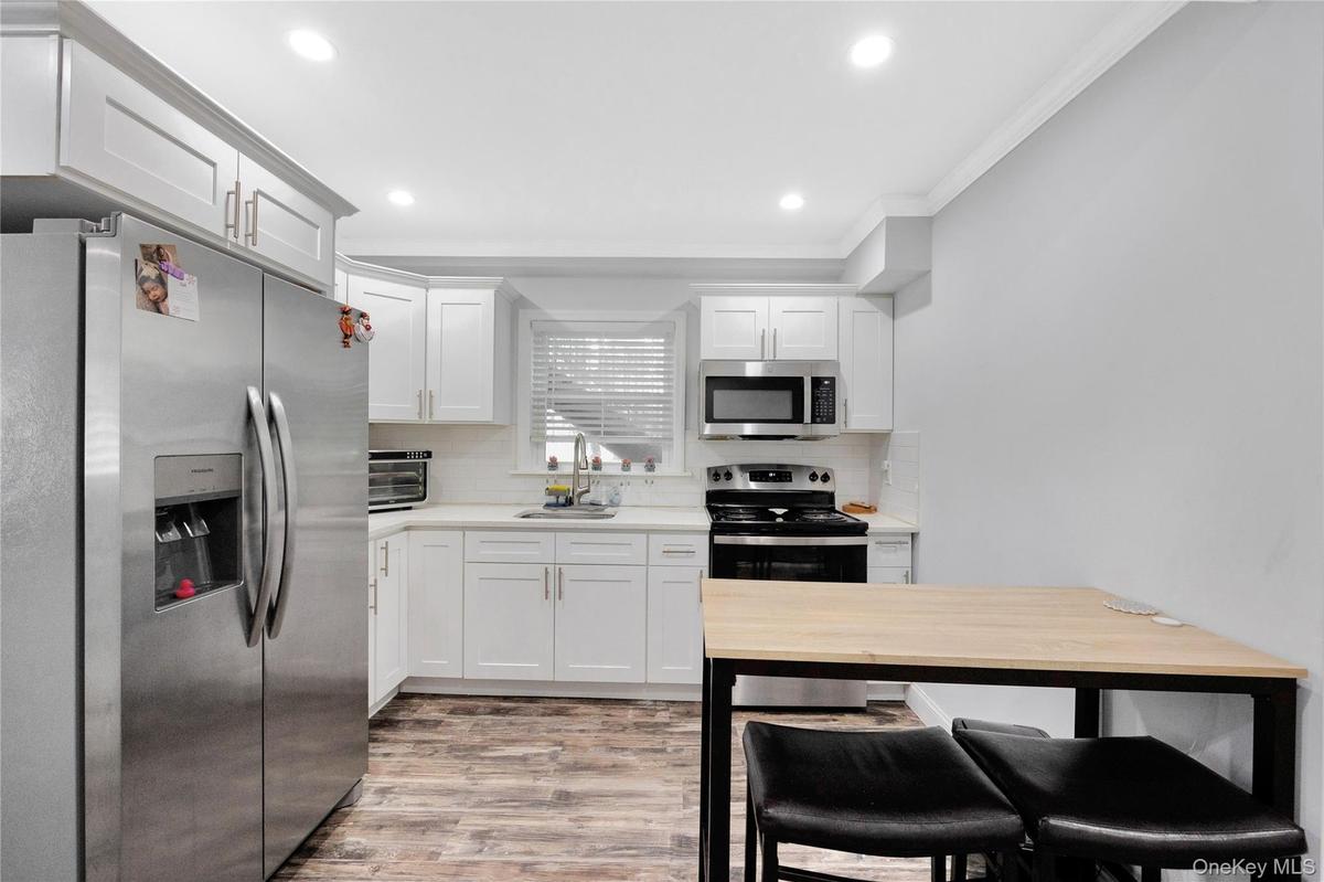Kitchen featuring stainless steel appliances, ornamental molding, decorative backsplash, recessed lighting, and white cabinetry